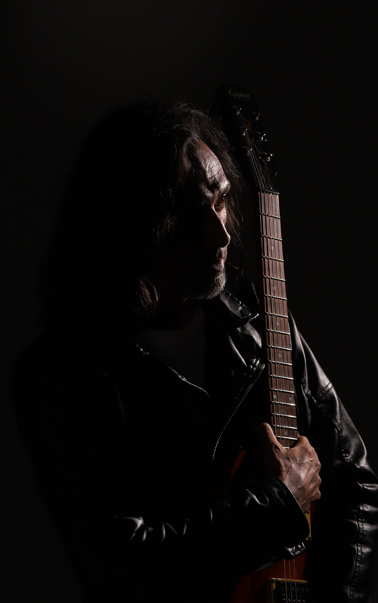 Mario Magno en penumbra junto a una guitarra eléctrica